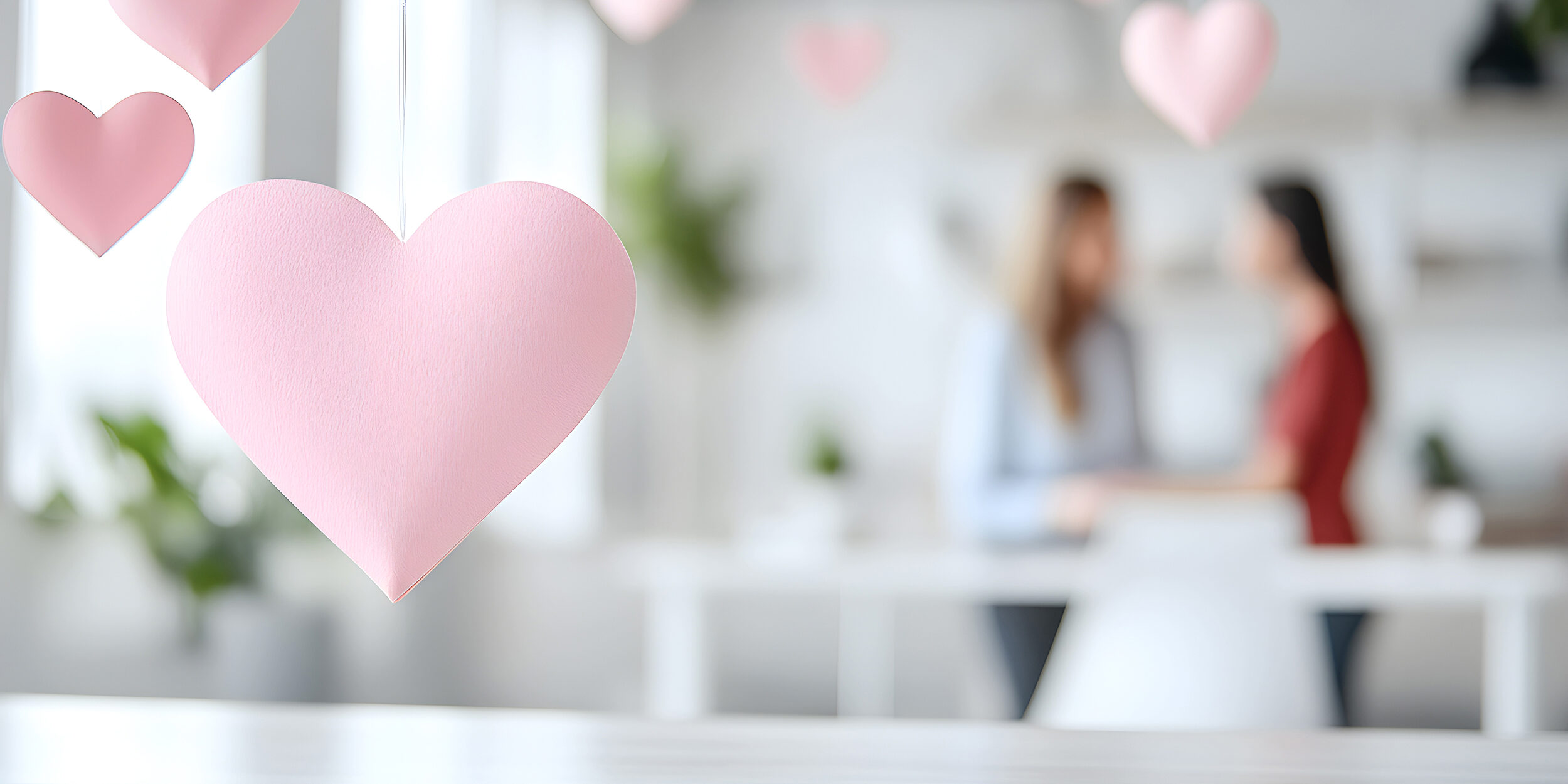 Close-up of hanging pink paper hearts with blurred people in the background in a cozy environment. Perfect for promoting relationship themes or Valentine's Day decor ideas. Selective focus.