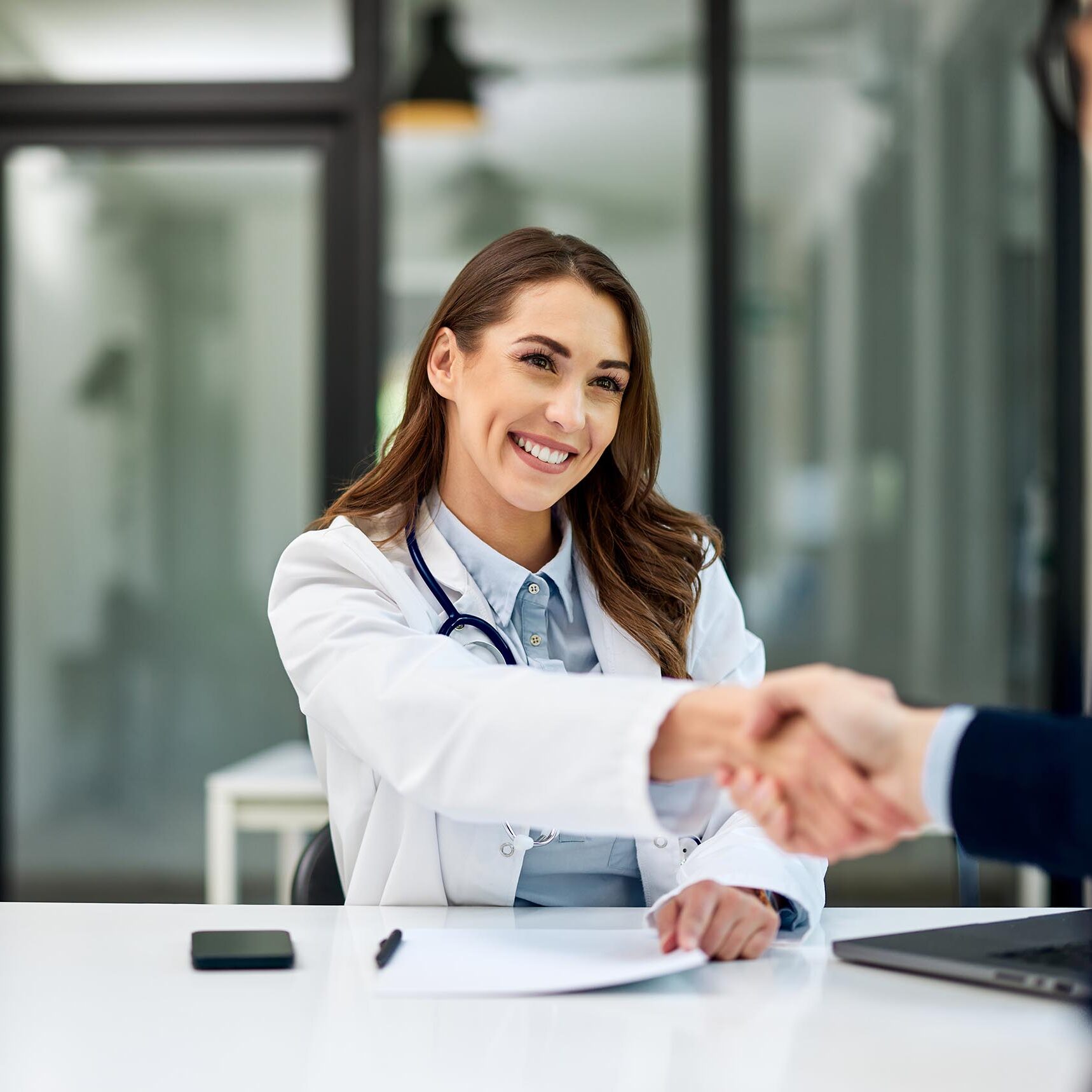 A smiling female patient sits at the office table and handshakes with a male patient.
